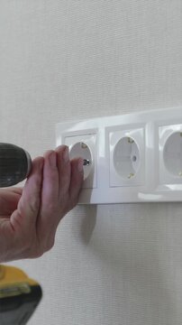 Electrician hands installing white faceplate frame over four wall sockets