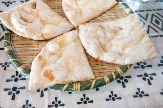 Fresh baked Indian naan flatbread slices served on a woven plate.