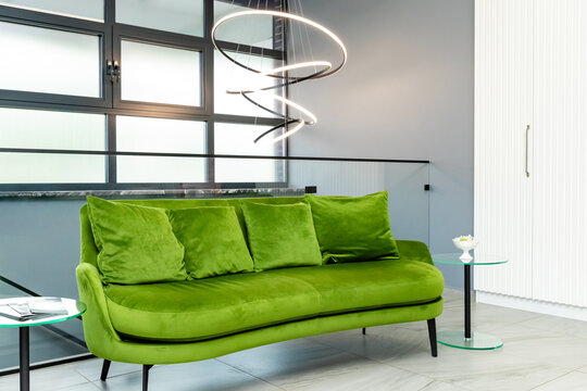 Modern green velvet sofa with decorative cushions in a stylish interior featuring a contemporary light fixture and minimalist design elements