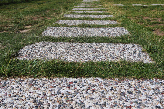 Low angle view of a stone path made of square gravel stepping stones leading through green grass in a garden