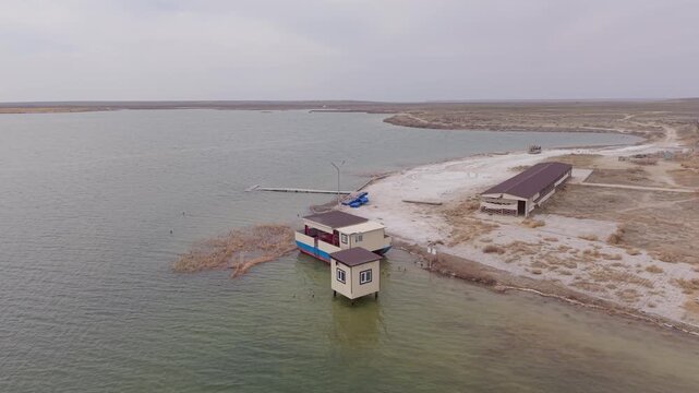 Aerial view of the Aral'sk shoreline featuring small structures and a pier along the water in Aral, Kyzylorda Region, Kazakhstan.