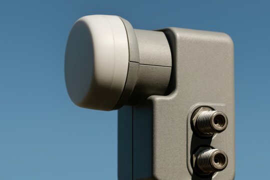Close-up of satellite dish LNB receiver with twin coaxial connectors mounted against clear blue sky