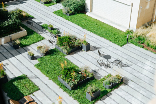 The courtyard features stone pathways surrounded by green plants and planters. Several black chairs and tables are arranged in the space, creating a seating area for outdoor use