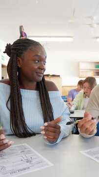Young female and male high school students smiling and talking while dishonestly cooperating during an important science test, cheating by looking at each other's papers to find the answers