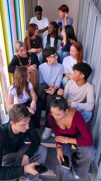 Large group of multiethnic high school students sitting together on a colorful staircase, talking and using their smartphones while having fun together, representing youth culture and social life
