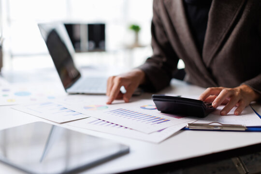 Business person working on financial analysis, calculating data, and reviewing corporate reports with a laptop and tablet, focusing on investment, accounting, and economic planning