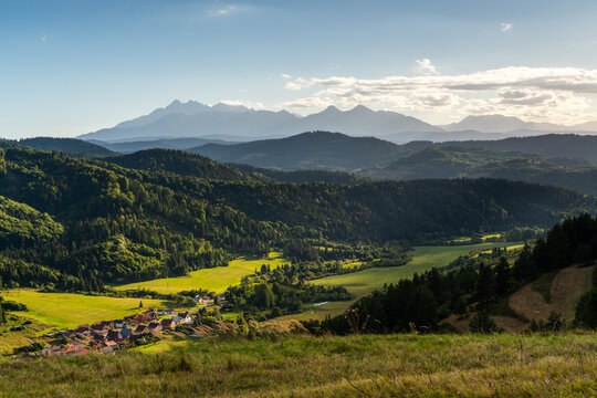 View of Lesnicke sedlo overlooking the village of Velky Lipnik, surrounded by lush meadows, dense forests, and distant mountains under a soft sky in Velky Lipnik, Presovsky kraj, Slovakia.