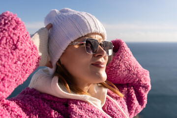 Young woman wearing pink fleece and white beanie enjoys warm sunny day by the blue ocean shore © svetograph