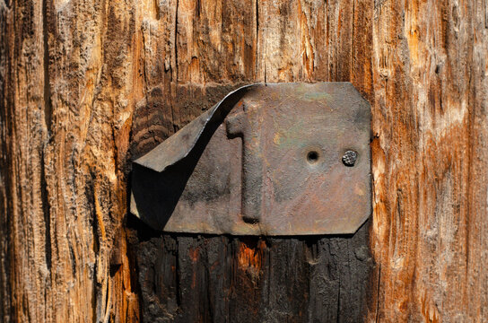 Old weathered wooden pole with a rusty metal tag displaying the number one, rustic textured background.