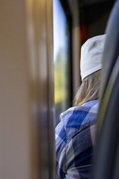 Woman dozes peacefully on train viewed from behind while traveling toward Karkonosze mountains Poland. Concept of restful solo travel journey and quiet anticipation before hiking adventure begins.