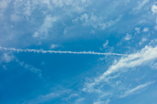 A clear blue sky with white clouds and a visible contrail stretching across the horizon. The scene conveys a sense of tranquility and openness.