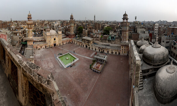 View of the historic Wazir Khan Mosque with its ornate minarets, central courtyard, and surrounding domes in the dense urban landscape of Lahore, Punjab, Pakistan.