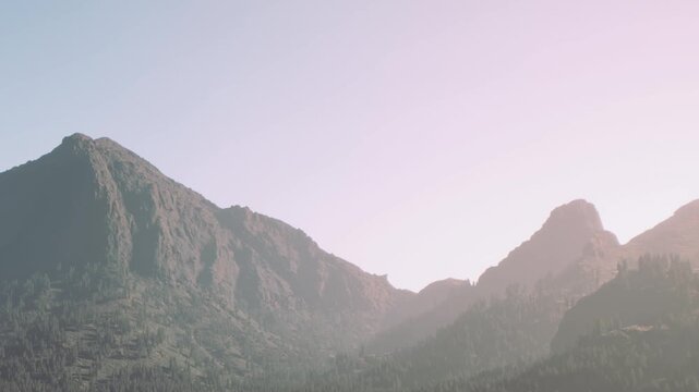 The scene shows mountains with a clear sky. The sun is shining on the peaks. This is a daytime view in a natural setting. There are no clouds in sight.