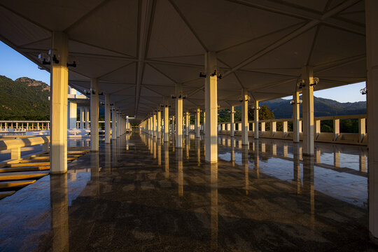 View of the geometric pillars and reflective floor of Faisal Masjid at sunset with the Margalla Hills in the background in Islamabad, Islamabad Capital Ter, Pakistan.