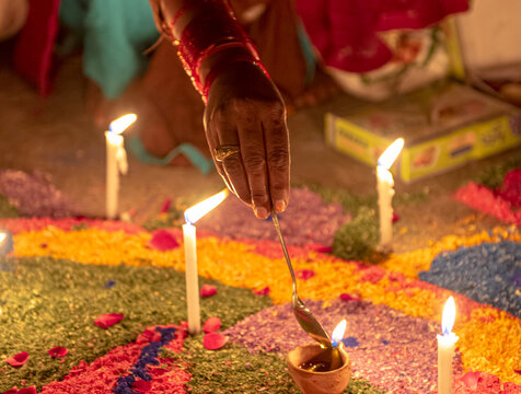 View of a person's hand using a spoon to light a diya on a vibrant rangoli pattern decorated with lit candles during the Diwali festival in Rahim Yar Khan, Punjab, Pakistan.