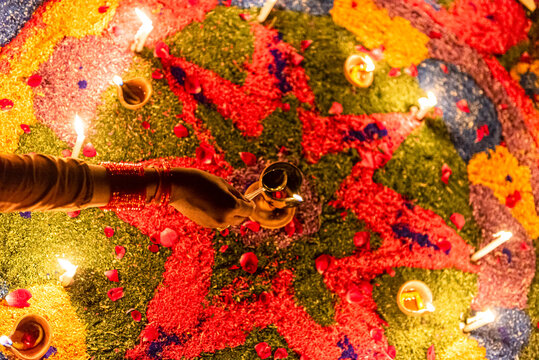 View of a hand holding a lit diya over a colorful rangoli pattern made of flower petals and powder, illuminated by candles during the Diwali festival in Rahim Yar Khan, Punjab, Pakistan.