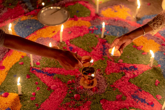 View of hands lighting traditional clay diyas on a colorful floral rangoli pattern during the Diwali festival in Rahim Yar Khan, Punjab, Pakistan.