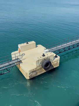 View of a concrete pier platform with a metal walkway and a tire bumper floating in the turquoise sea in Canakkale, Canakkale, Turkiye.