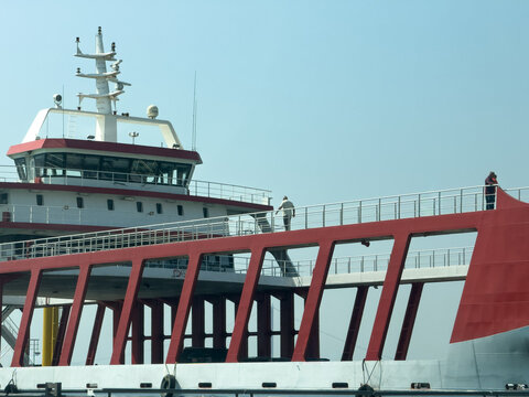View of a ferry boat with a red metal structure and white bridge, featuring people walking on the deck under a clear sky in Canakkale, Canakkale, Turkey.