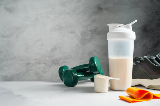 Protein shake and whey powder with dumbbells and running shoes, fitness nutrition concept, copy space