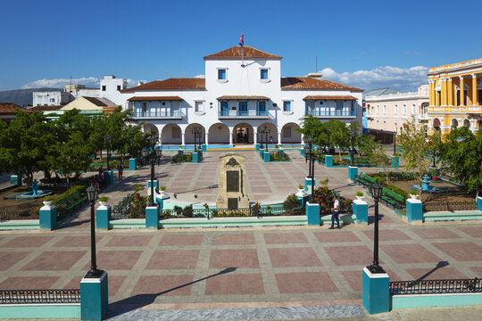 View of the historic Ayuntamiento de Santiago de Cuba city hall building overlooking the paved Parque Cespedes with trees and a monument in Santiago de Cuba, Santiago de Cuba, Cuba.
