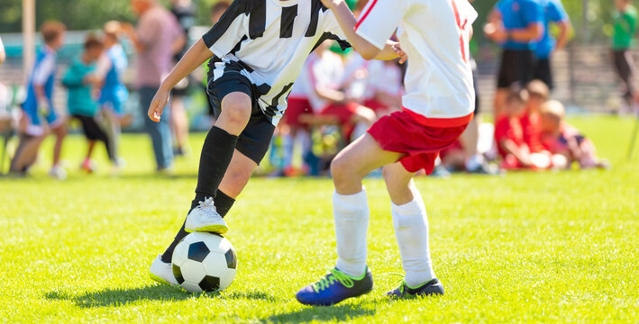 Junior Soccer Players in Striped and Red Kits Battling for Ball Possession - Action Shot of Competitive Youth Football League Match on Pitch
