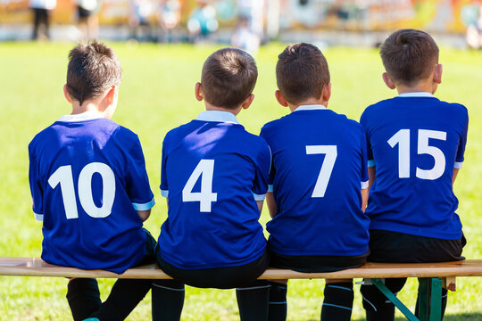 Happy Boys in Blue Soccer Team. Junior Soccer Substitutes in Blue Shirts Numbers 10, 4, 7, and 15 Sitting on Wooden Bench - Youth Football Team Support During Match