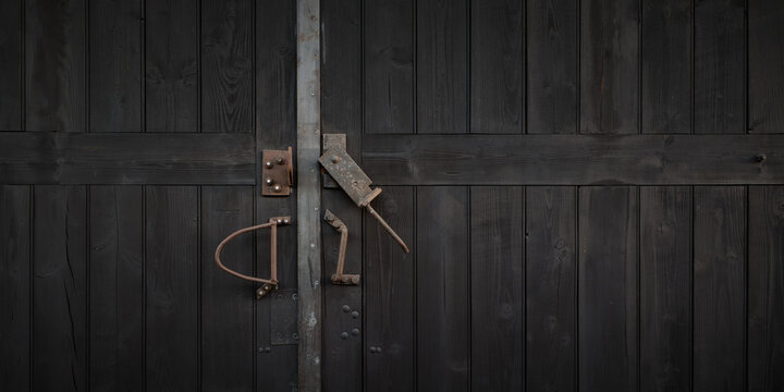 Dark wooden double door with a rusty metal latch and aged hardware, framed as a wide rustic background with useful space for text and themes of security and closed access.