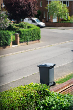 Black wheelie bin placed on residential street pavement for household waste collection