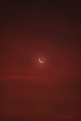 A serene crescent moon glowing against a rich red twilight sky, evoking a calm and mystical night scene © pak