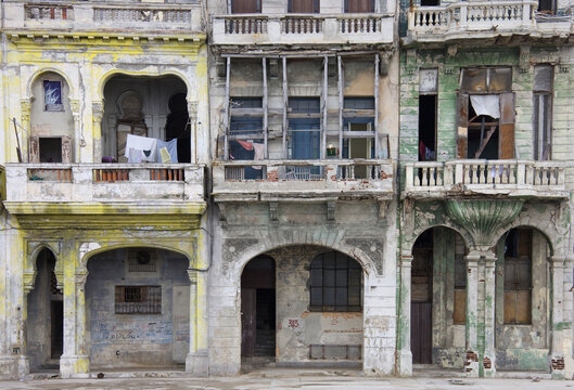 View of weathered colonial buildings with peeling paint, arched doorways, and balconies in Havana, Havana, Cuba.