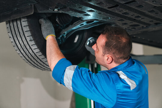 Electric vehicle battery car service Automotive mechanic inspecting vehicle undercarriage and tire with focused expression in repair garage setting