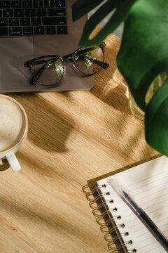Home office workspace with open notebook, coffee and eyeglasses on wooden desk, top view with copy space