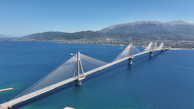 High aerial view of the impressive cable stayed bridge connecting shores with mountains in the background under clear blue sky.