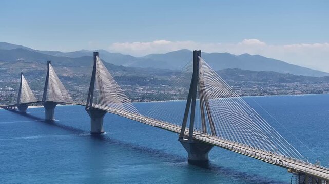 High aerial view of the grand multi-span cable bridge spanning the blue sea under bright daylight with mountains in the background.