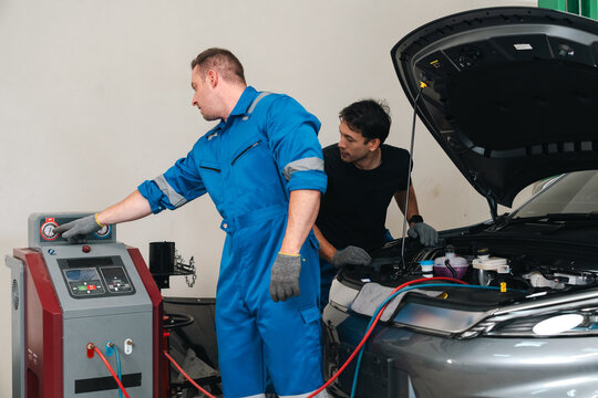 Electric vehicle battery car service Automotive technician in blue coverall operates service equipment beside open car hood indoors