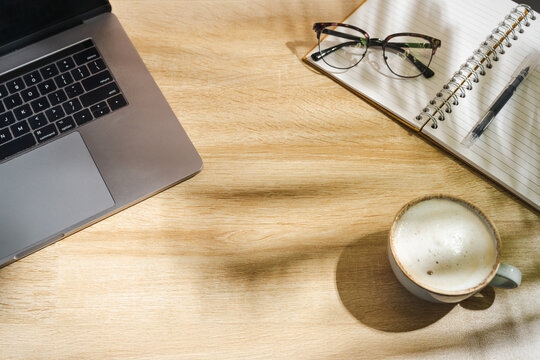 Home office workspace with notebook, coffee and eyeglasses on wooden desk, top view with copy space