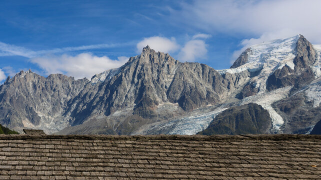 View of the melting glaciers at the Mont Blanc massif seen behind a traditional wooden shingle roof under a clear blue sky in Chamonix, Auvergne-Rhone-Alpes, France.