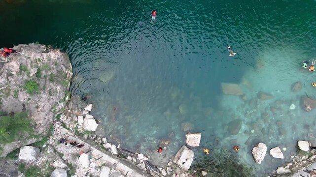 Rising aerial view of people swimming in the pristine turquoise water of Swaik Lake in Punjab, Pakistan.