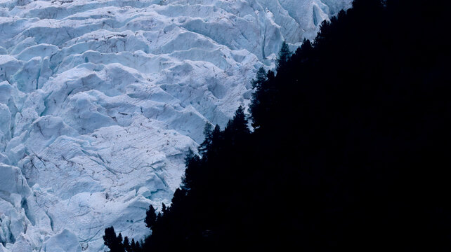 View of the melting glaciers at the Mont Blanc massif with deep blue ice crevasses contrasting against a dark forest edge in Chamonix, Auvergne-Rhone-Alpes, France.