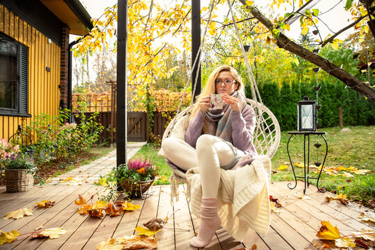 A mid adult woman enjoys a warm drink in a swinging macrame chair on a cozy autumn patio. Mental clarity outdoors during a mindful routine.