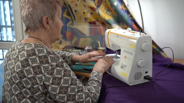 Senior woman sewing on a sew machine. Craft table