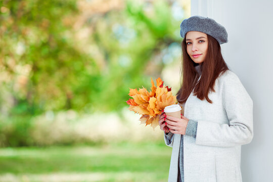 Autumn portrait of a beautiful happy smiling woman with yellow maple leaves in a gray beret in the park
