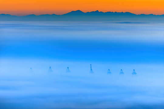 View of harbor cranes rising above a thick layer of morning fog at sunrise with mountains in the background in Cape Town, Western Cape, South Africa.