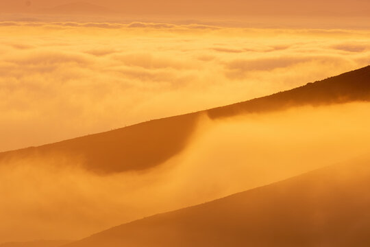View of Table Mountain partially obscured by thick golden clouds during sunset in Cape Town, Western Cape, South Africa.