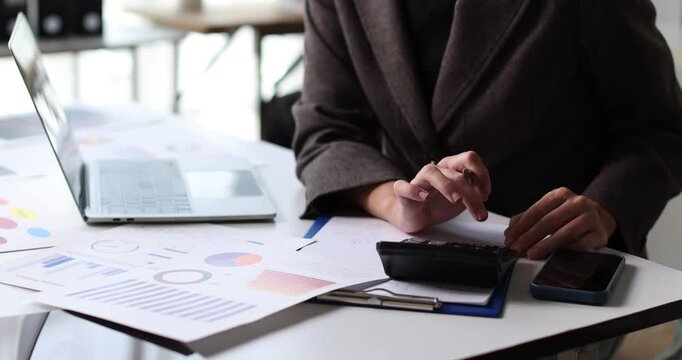 Business professional analyzing financial data and charts on paper documents, using a calculator and laptop, working on accounting, finance, and investment planning