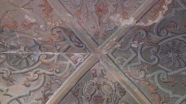 Ornate painted Baroque ceiling panels with peeling plaster and floral scrollwork fill the frame in the Majolica Cloister of Santa Chiara.