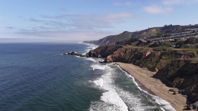 Drone video captures Mussel Rock Park beach in Daly City, California, revealing dramatic cliffs, rolling waves, sand, and scenic coastline in crisp morning sunlight with sweeping sky perspective.