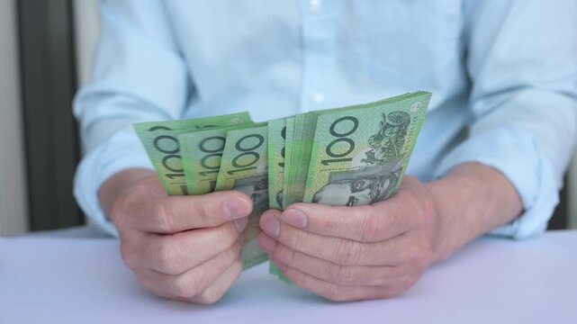Saving money investment and financial planning concept. A man counting hundred and fifty Australian dollar bills in cash on hand as payment, savings, business funds, dividends, wealth.