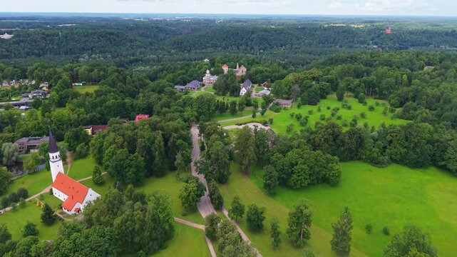 Aerial view of historic Krimulda Lutheran Church surrounded by lush green countryside, forests and meadows within Gauja National Park in Latvia